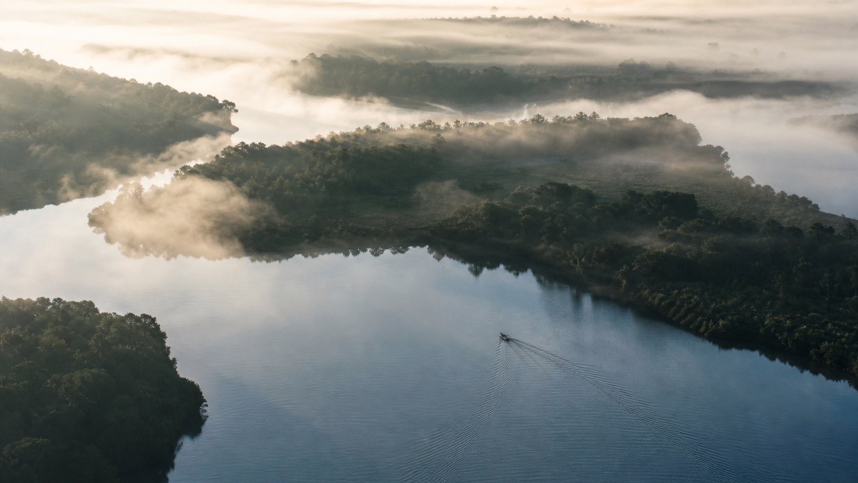 A small boat moving through a wide river landscape